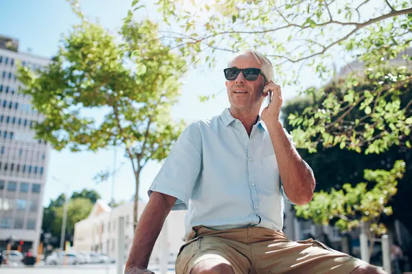 Mature man sitting outdoors in the city making a phone call