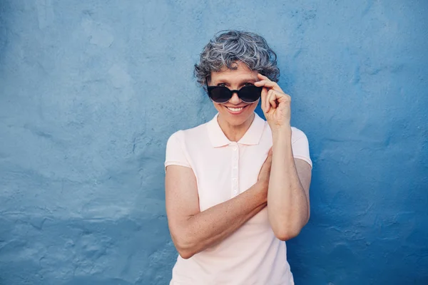 Smiling mature woman peeking over sunglasses