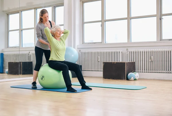 Female trainer helping senior woman exercising in gym