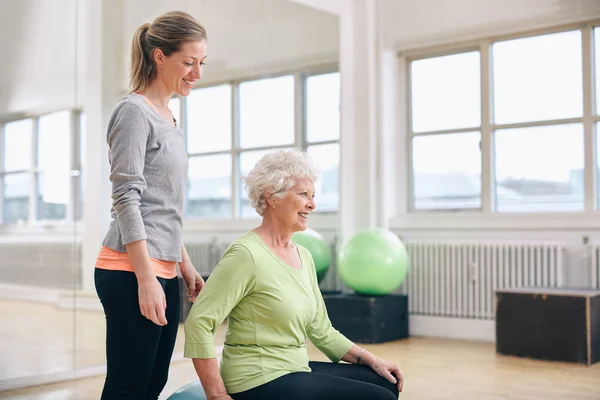 Female instructor assisting senior woman exercising in gym