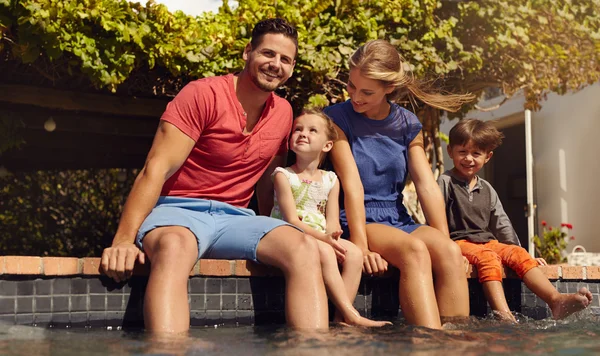 Beautiful young family sitting next to swimming pool