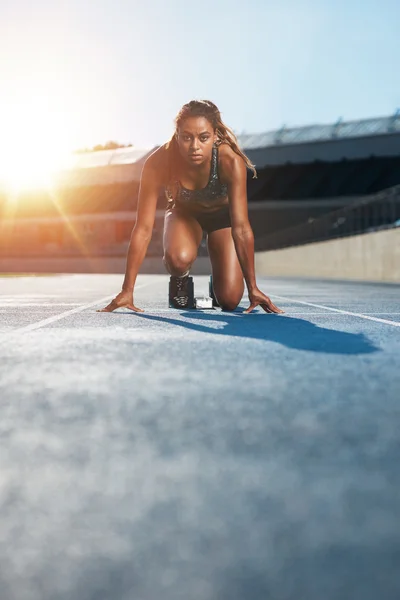 Young female sprinter in start position on racetrack