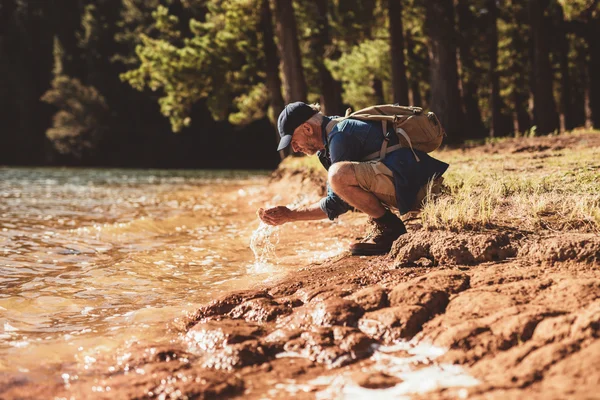 Mature man washing face from lake water