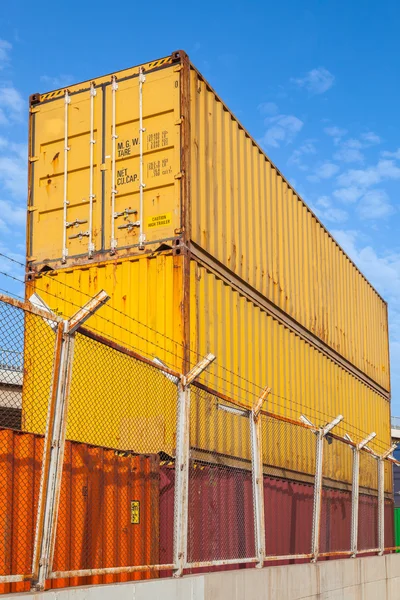 Metal cargo containers are stacked under blue cloudy sky