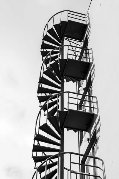 Outdoor metal spiral ladder on the wall, black and white photo