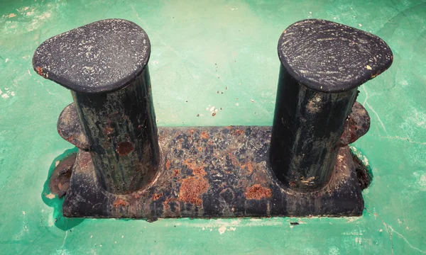 Old black rusted bollard on green ship deck