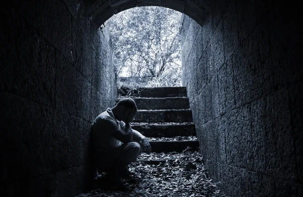 Young sad man sitting inside of dark stone tunnel