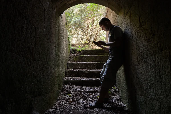 Young man works on a smart-phone in dark tunnel