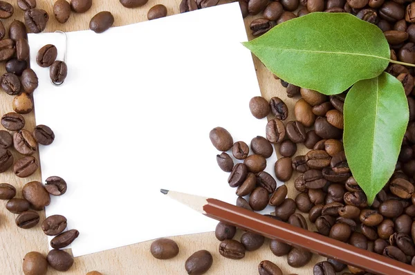 Coffee beans,cup of coffee, green leaves, white blank and pen on wooden desk