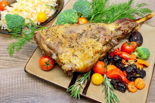 Baked leg of lamb with vegetables and herbs on a plate on a wood