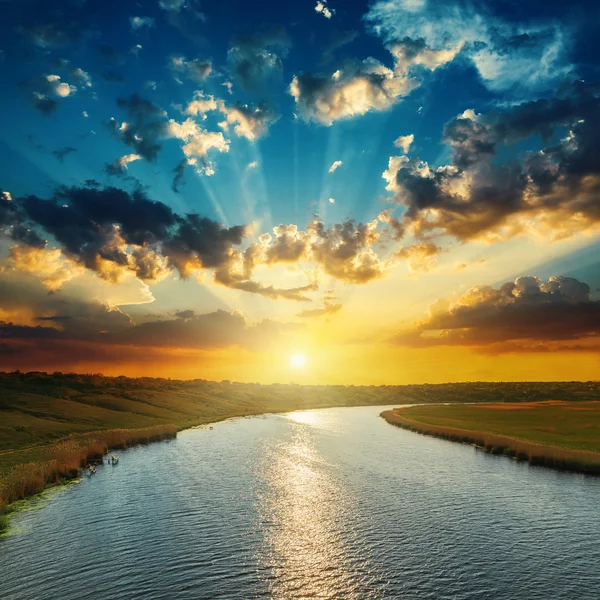 Sunset with clouds, light rays over river with reflections