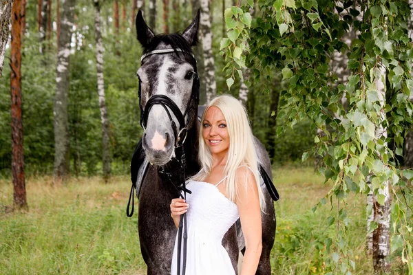 Beautiful blonde woman and gray horse in forest