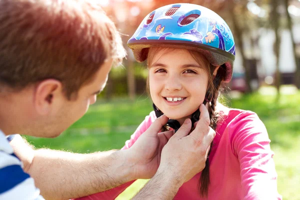 Father teaching brave daughter to ride bicycle putting on safety helmet