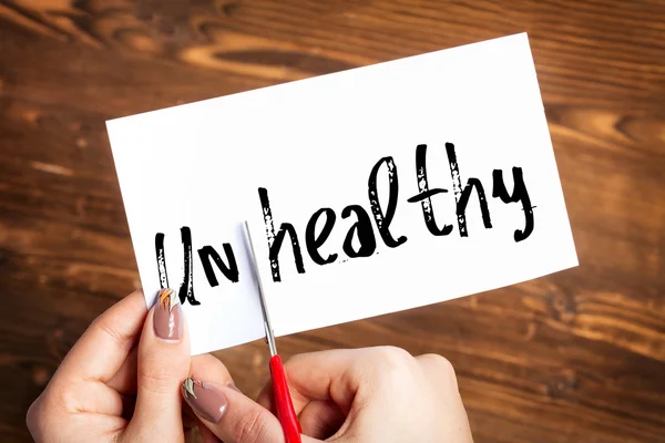 Woman hands cutting card with the word unhealthy