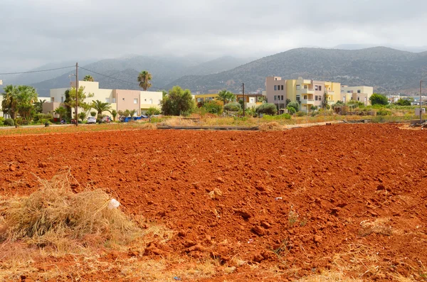 View of red arable land, Malia town and mountain.