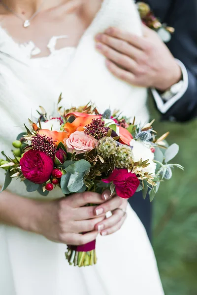 Groom  holding shoulder of bride with red rose bouquet in hands
