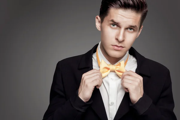 Portrait of young trendy groom with yellow bow-tie on gray backg