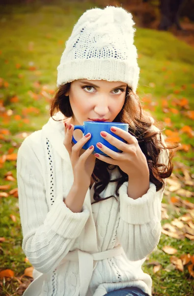 Young beautiful girl drinking a hot drink in the park