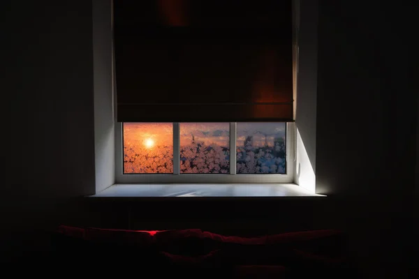 The window in the room with a red sofa and blinds