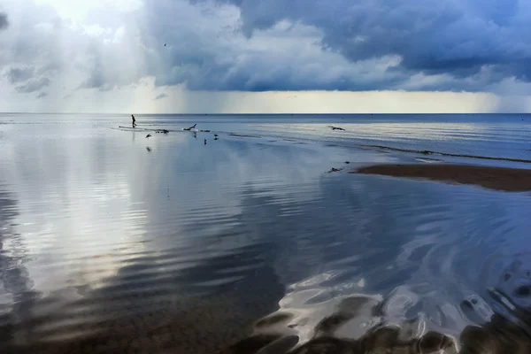 A man walks on the beach with reflection of clouds in the sea