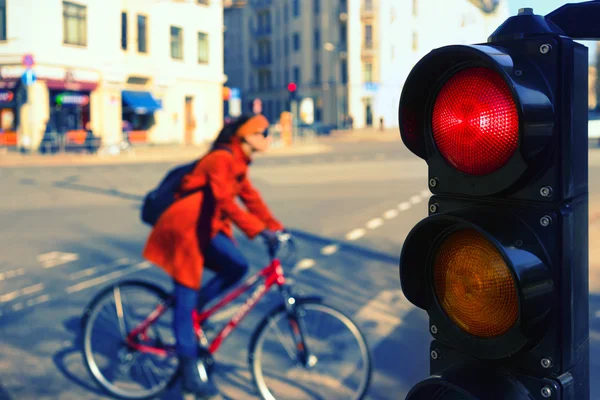 The girl on a bicycle on a city street at a red traffic light