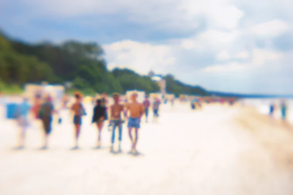 People at the weekend walk on the beach in summer. Blurry