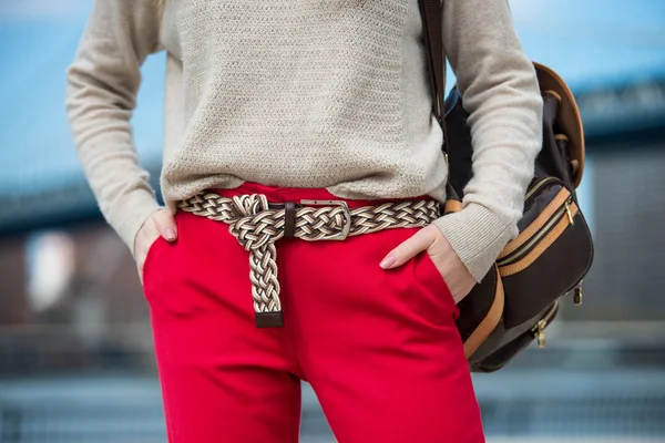 Fashionable women`s casual spring outfit with red pants, cardigan, modern belt and shoulder bag