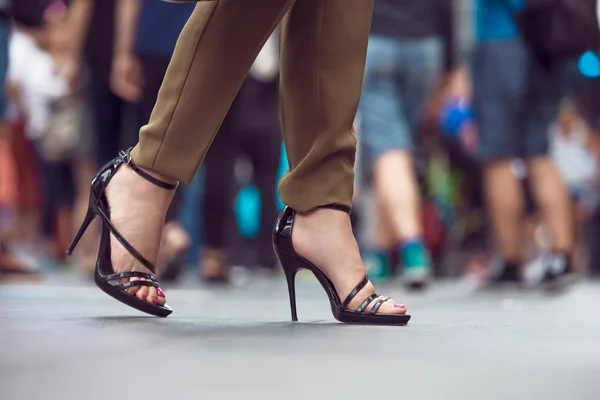 Woman wearing black high heels summer shoes walking in the city crowd. Woman feet making step on city street. Female legs and feet with shoes close-up.