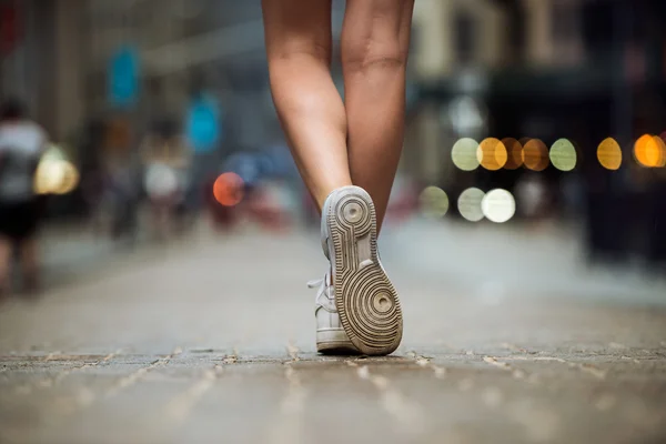 Female feet wearing sneakers running in city street. Woman with beautiful legs running in city at morning.