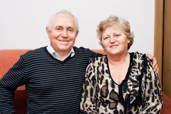 Happy senior couple sitting on the sofa at home and smiling. Happy senior man hug his senior woman wife.