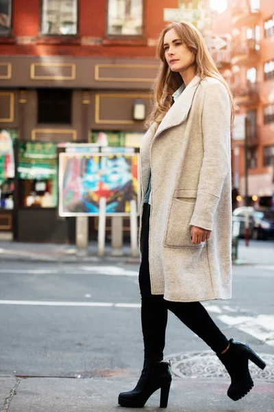 Young adult beautiful woman walking on city street wearing casual street style autumn outfit with grey jacket and black jeans