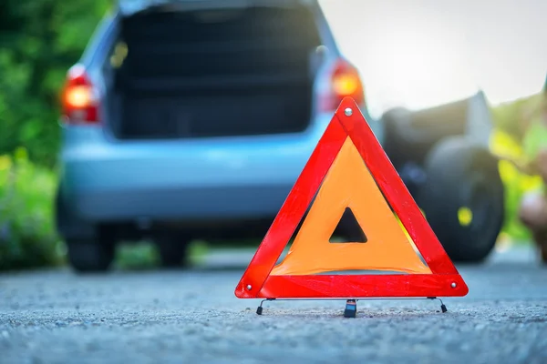 Changing the tire on a broken down car on a road with red warning triangle