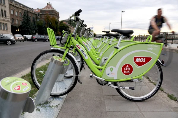 Bicycles on a public bike-sharing system\'s docking station. A man is  cycling on the background.