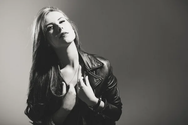 Black and white portrait of beautiful young woman in leather jacket on gray background, closeup