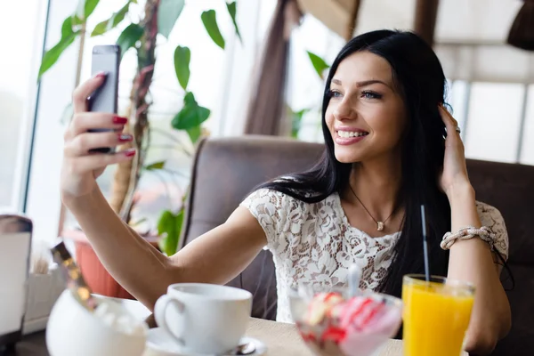 Selfie in restaurant: closeup image of beautiful brunette young female making selfy picture on mobile cell phone having fun happy smiling on coffee shop background