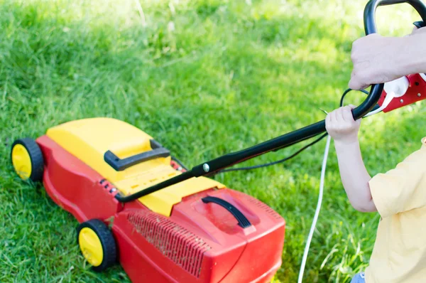 Together every little help counts: image of electric grass trimming or lawn mover machine operating or pushing by small boy or girl with adult behind on green copy space background