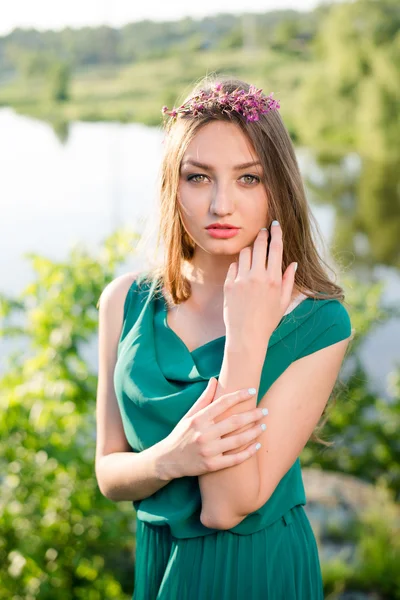 Portrait of pretty fairy: young lady cute girl having fun posing in green dress with pink wreath of flowers & sun light rays sensually looking at camera on summer outdoor copy space background