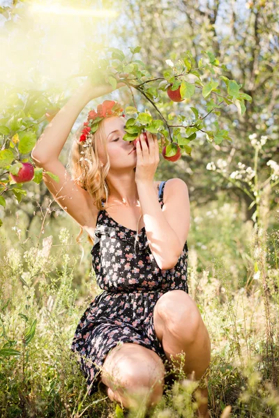 Blond girl smiling among red apples outdoors