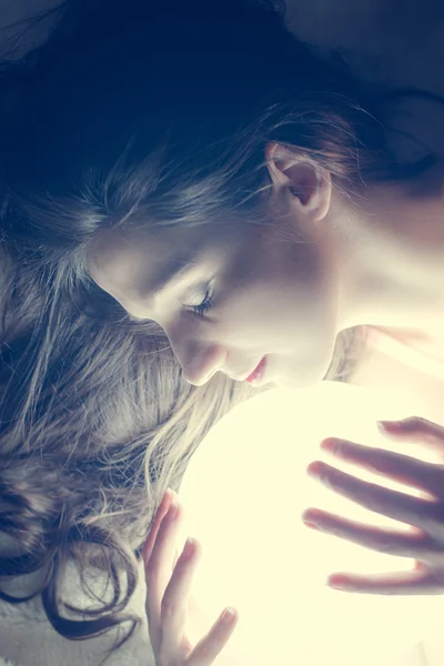 Closeup portrait of beautiful young woman holding ball of light and keeping eyes closed