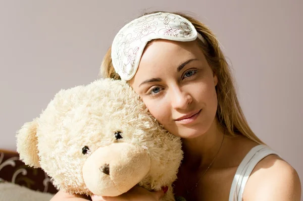 Woman blue eyes with sleep bandage hugging teddy bear