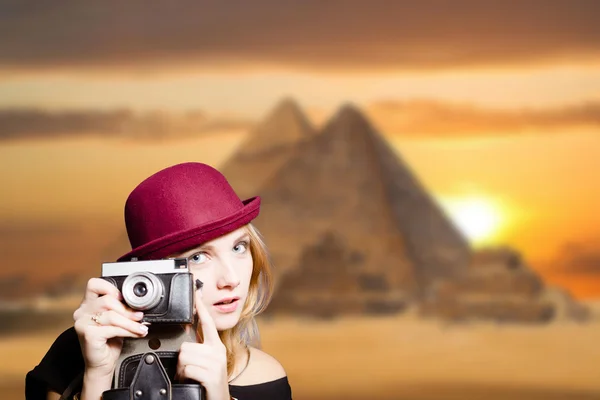 Girl in glasses with retro camera on Egypt pyramid background.