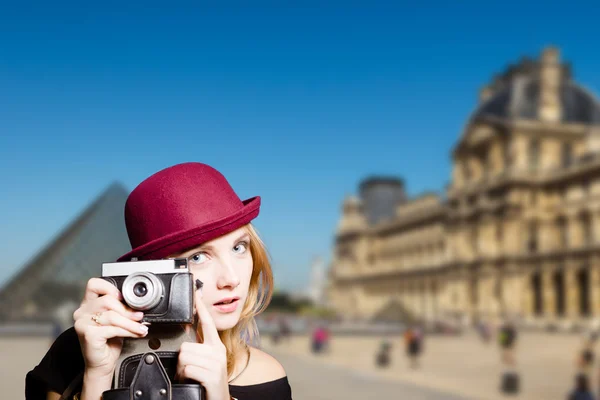 Romantic girl in sunglasses holding retro camera on Louvre background