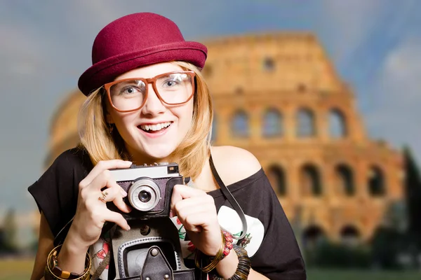 Pretty girl in glasses with retro camera on Colosseum background.