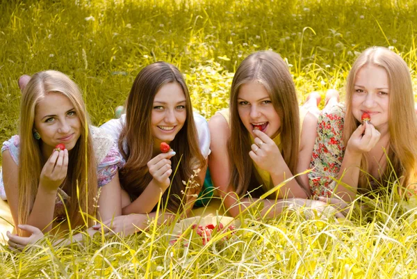 Four young friends having fun eating strawberry from huge bowl