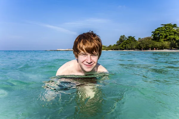 Red haired boy enjoys the crystal clear water in the sea