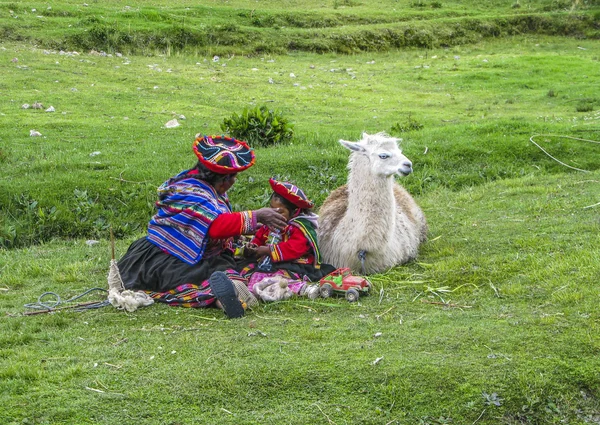 Indian woman with child and lama pose for tourists in Cuzco