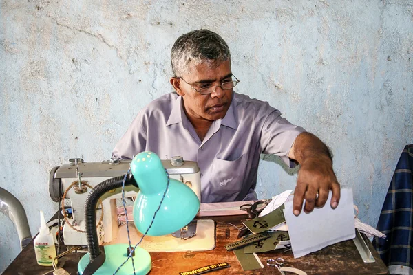 Sewer at the market is sewing name badges for customers