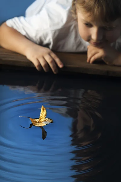 Boy play with leaf ship in water
