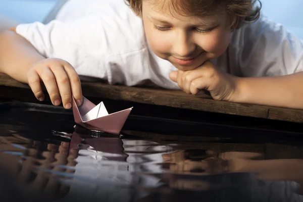 Boy play with leaf ship in water (focus on ship)