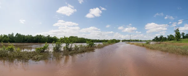 Panorama of a rural road completely inundated with flood waters, with pastureland on the left under water after heavy rains